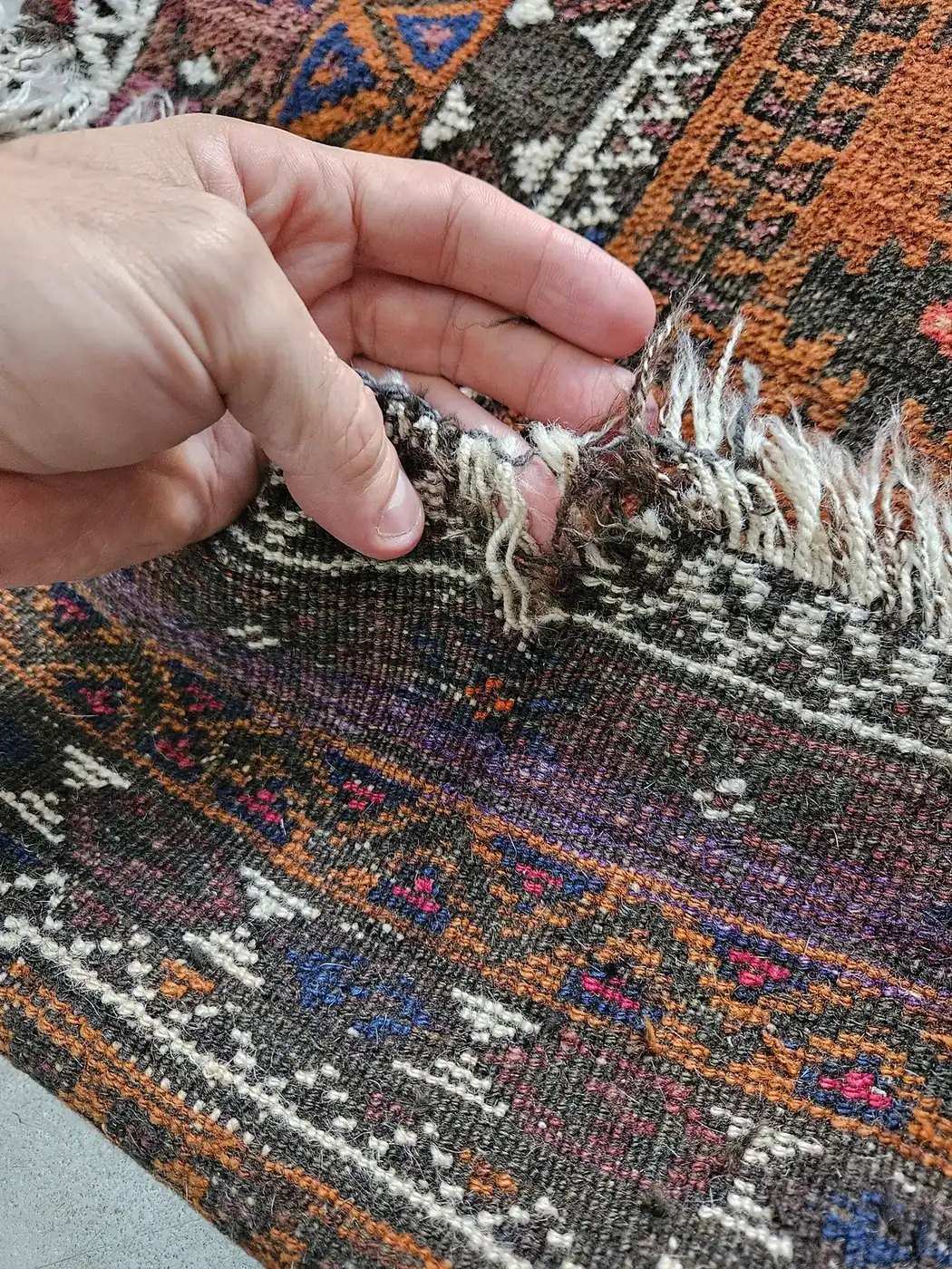 Hands hand-repairing the fringe of a colorful tribal rug at our own plant