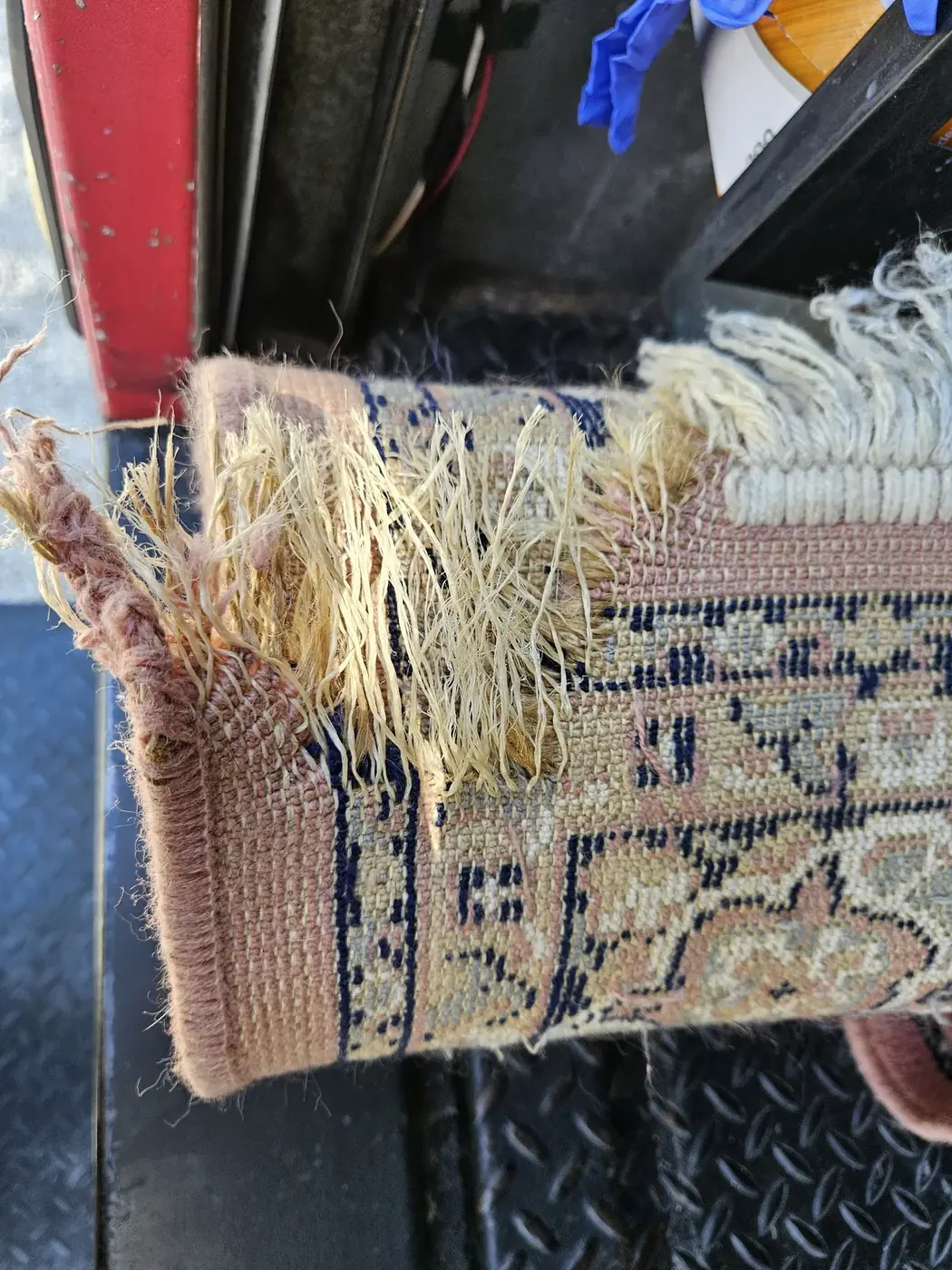 Worn, frayed fringe on the end of an Oriental rug awaiting repair