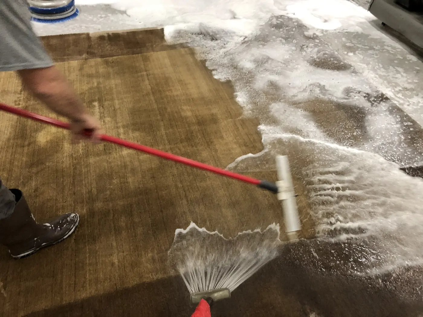A rug being rinsed by hand with a wash wand until the water runs clear